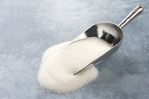 Silver scoop of sugar, spilling onto blue surface.